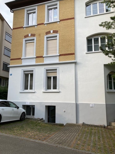 Multi-story residential building with a mix of yellow and white facades, multiple windows, and a small entrance area.
