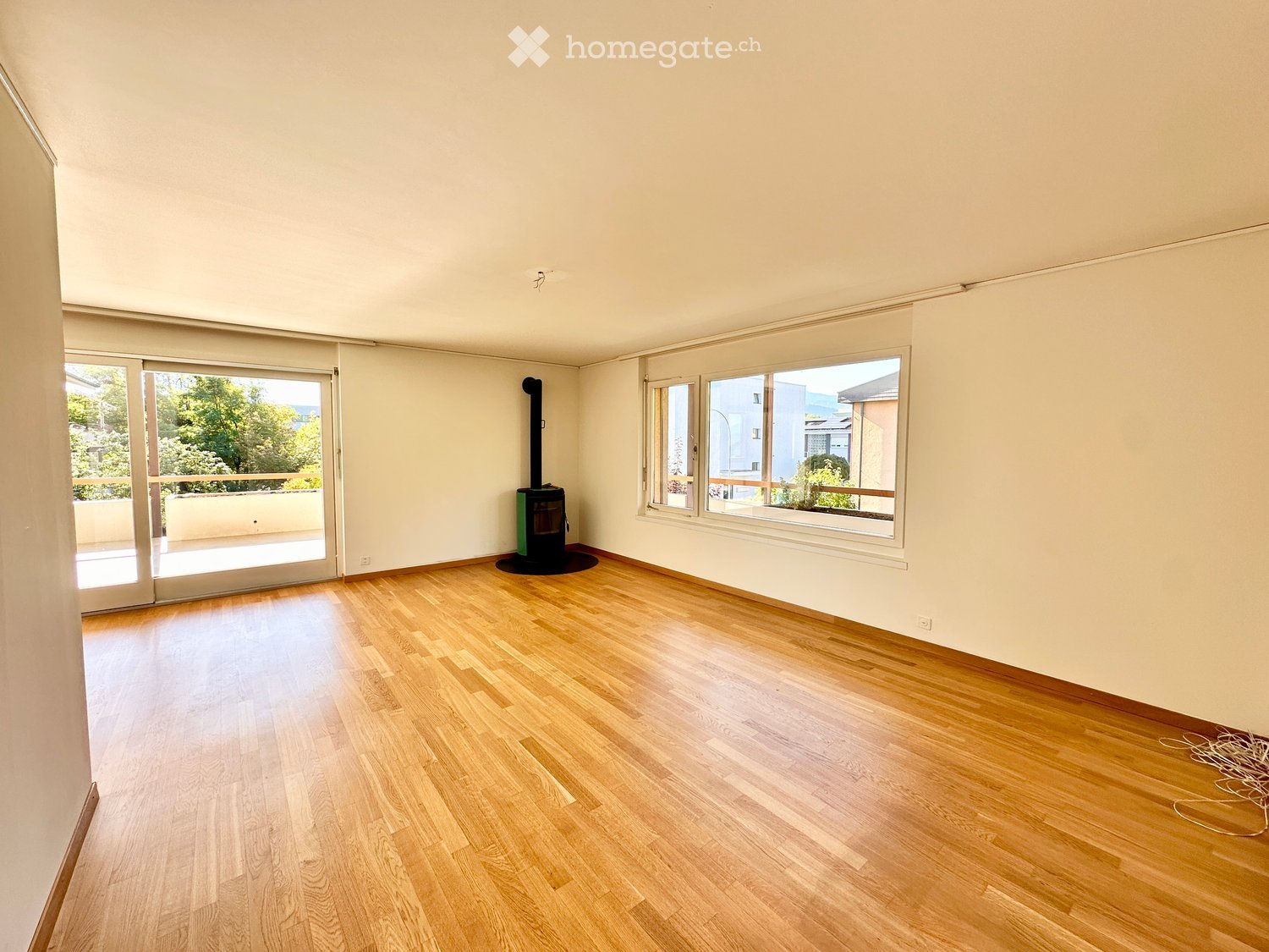 Empty room with wooden flooring, large windows, and a fireplace in the corner.