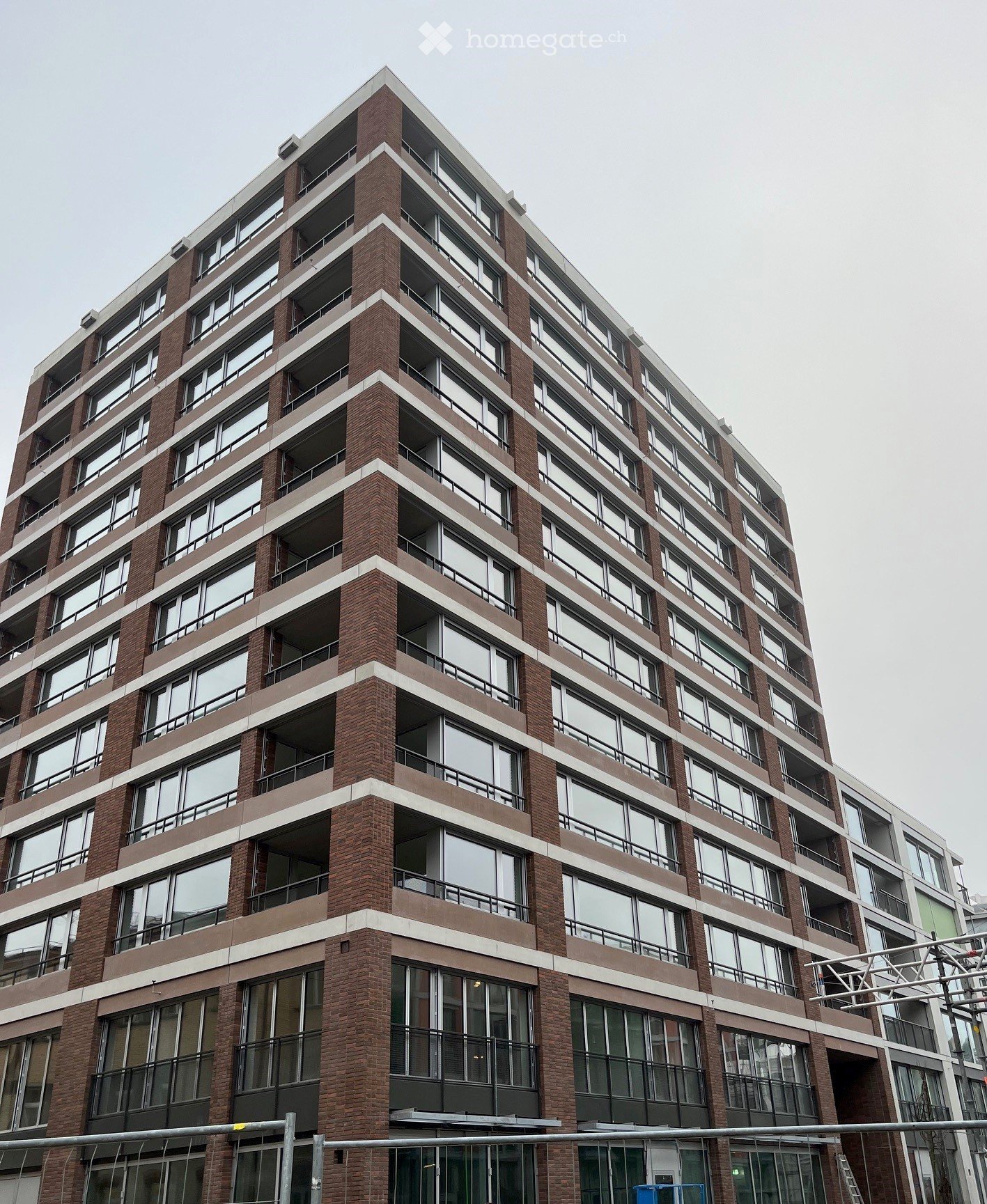 Modern multi-story building with large windows and balconies, featuring a brick facade and contemporary design.