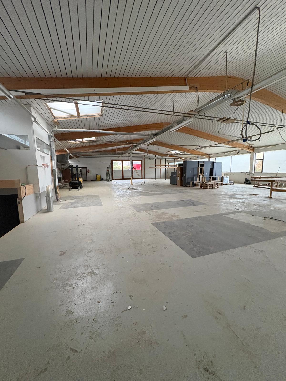Warehouse: large open space, wooden beams, windows, forklift, storage boxes, white walls, cement floor