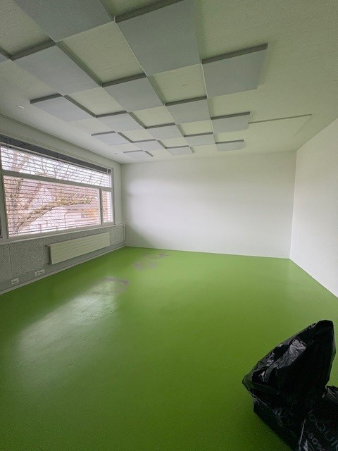Empty room with green floor, white walls, large window, and ceiling panels
