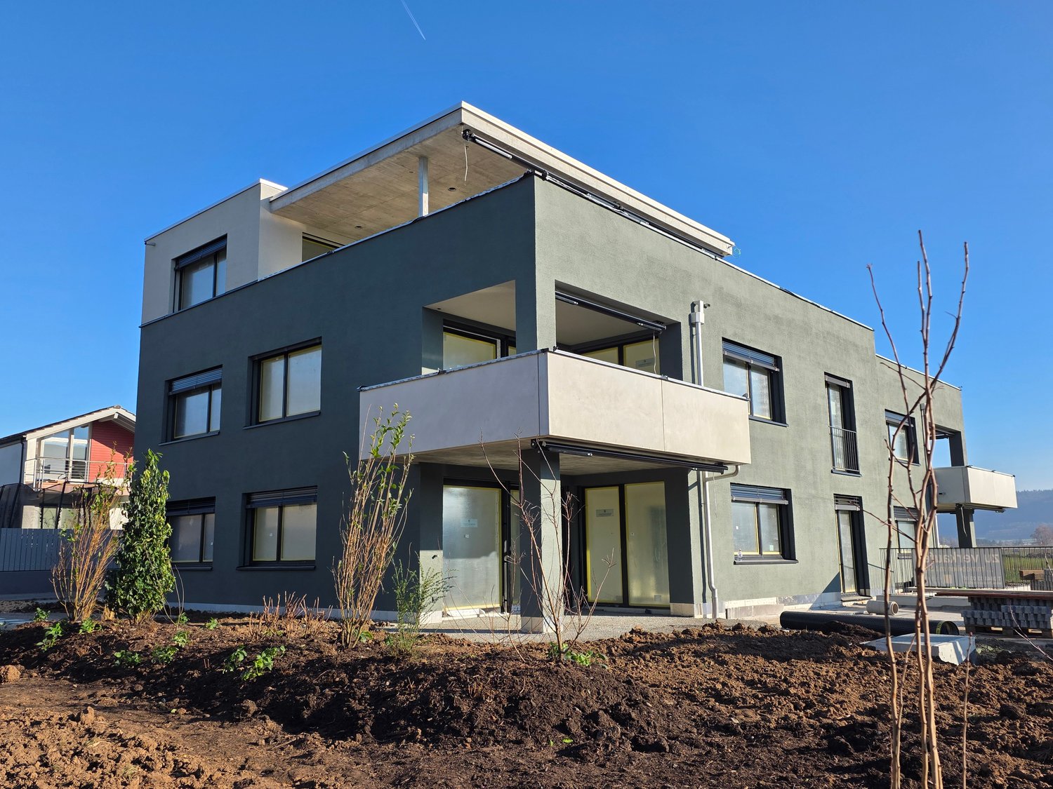 Two story modern house, gray color, multiple windows, balcony on second floor, glass doors, exterior garden