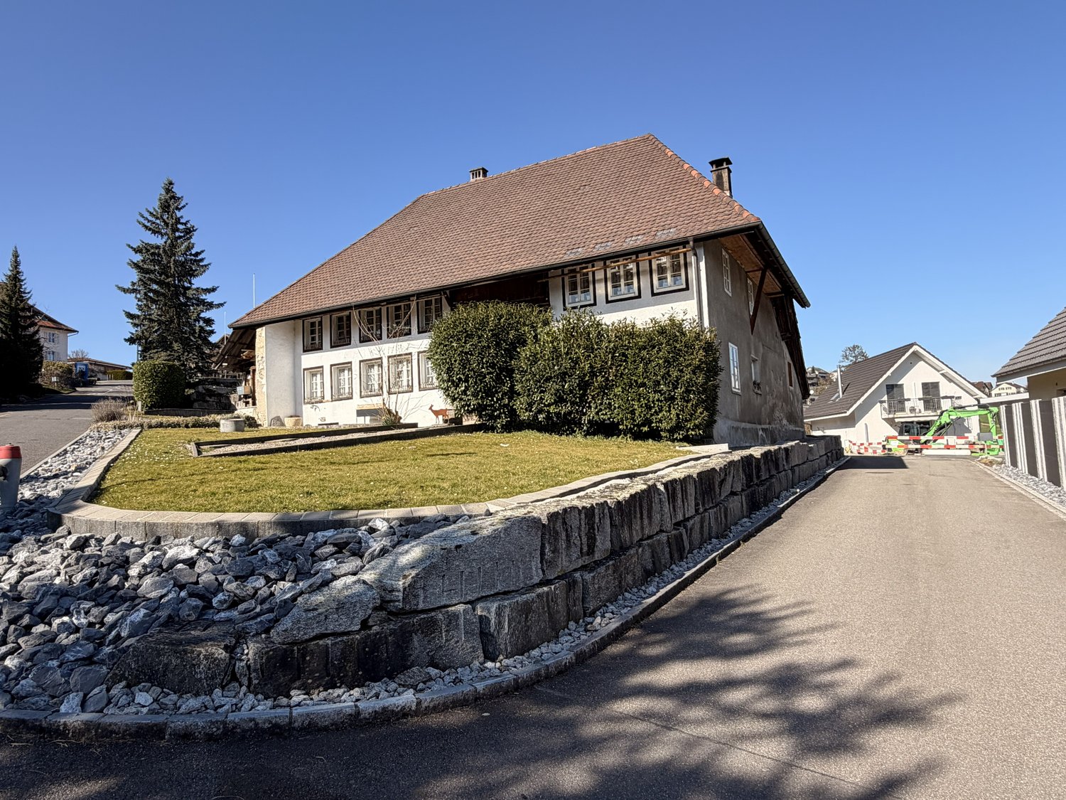 2 story house, brown roof, white walls, multiple windows, stone wall, driveway, green lawn, trees