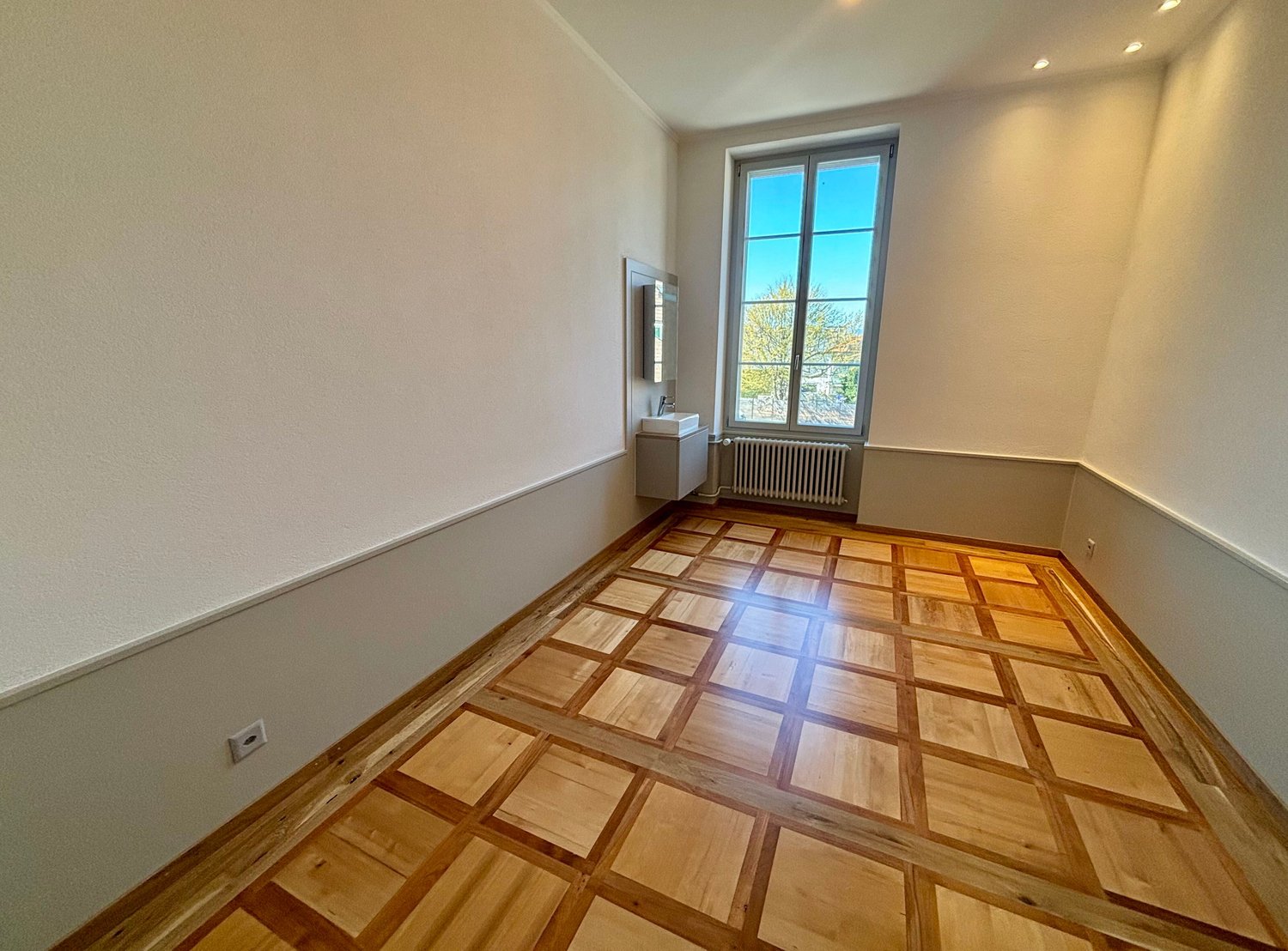 empty room, wooden parquet floor, white walls, window, radiator, sink, mirror