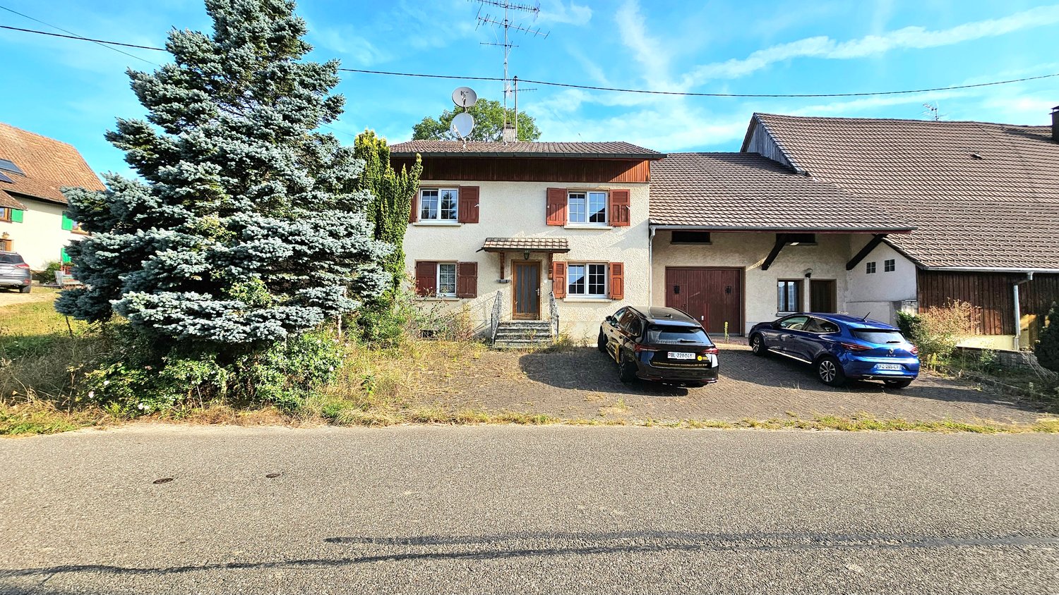 Detached house, two storeys, brown roof, white walls, wooden door, brown garage doors, trees, parking for two cars.