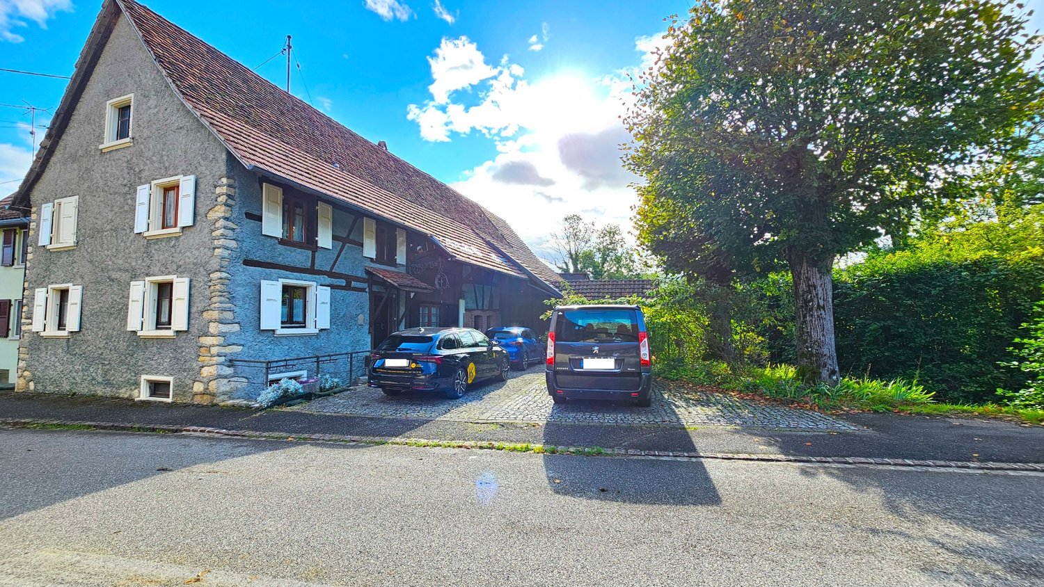 2 story house, grey walls, brown roof, stone detail, garage with two cars parked, shrubs, street in front