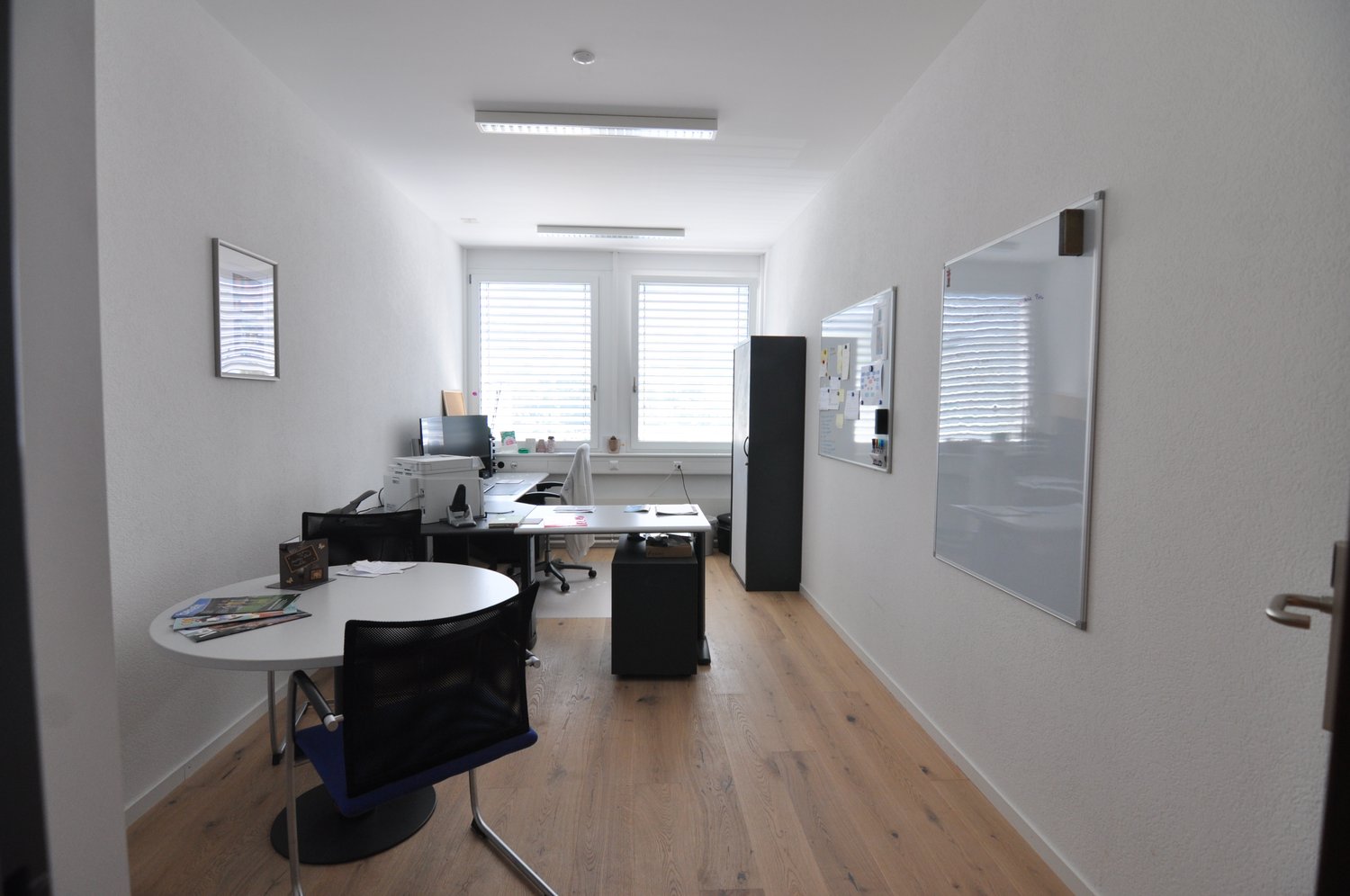 empty office with tables, chairs, computer, whiteboards, frames, wooden floor