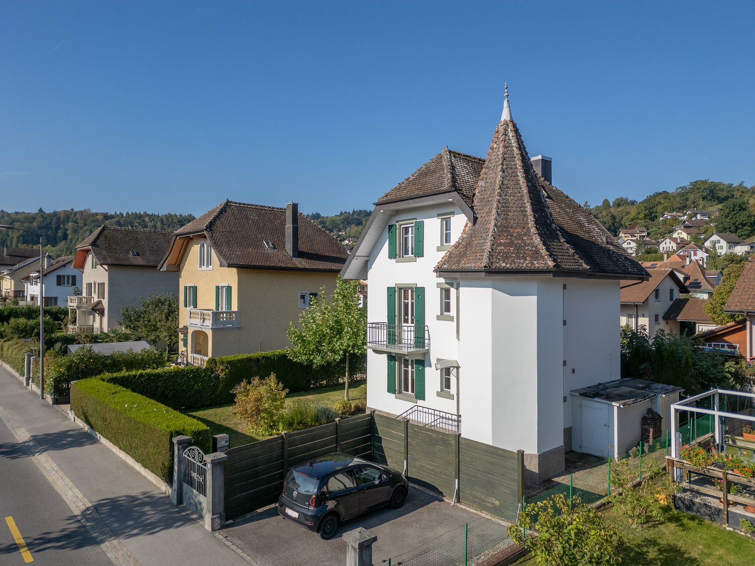 3 story house, white exterior, brown roof, green shutters, car parked in front, garden, hedges, neighboring houses