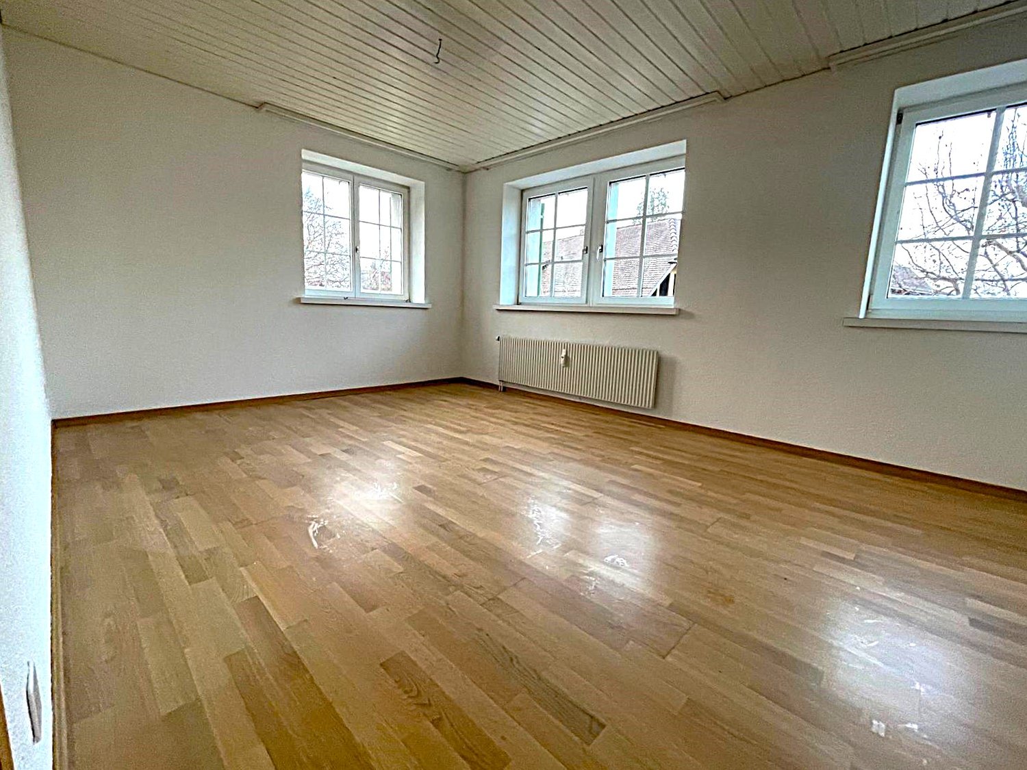 empty room, wooden floor, white walls, three windows, white ceiling, white radiator