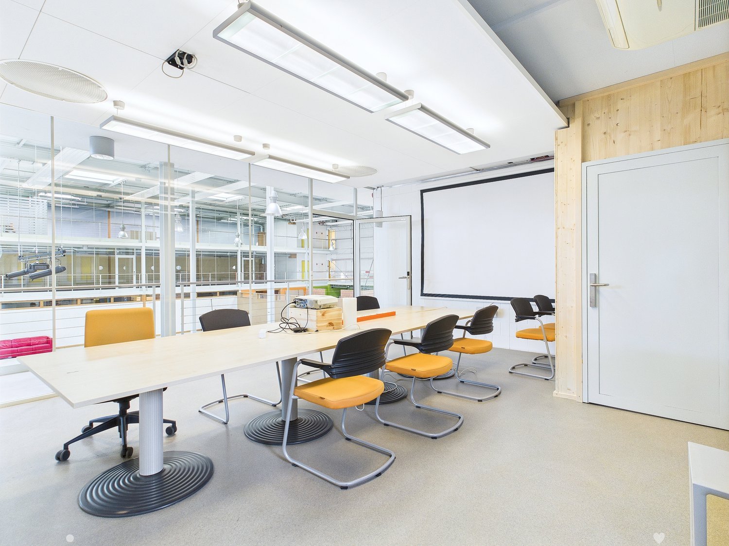 Modern office space with large conference table, swivel chairs, projector screen, and glass walls providing natural light