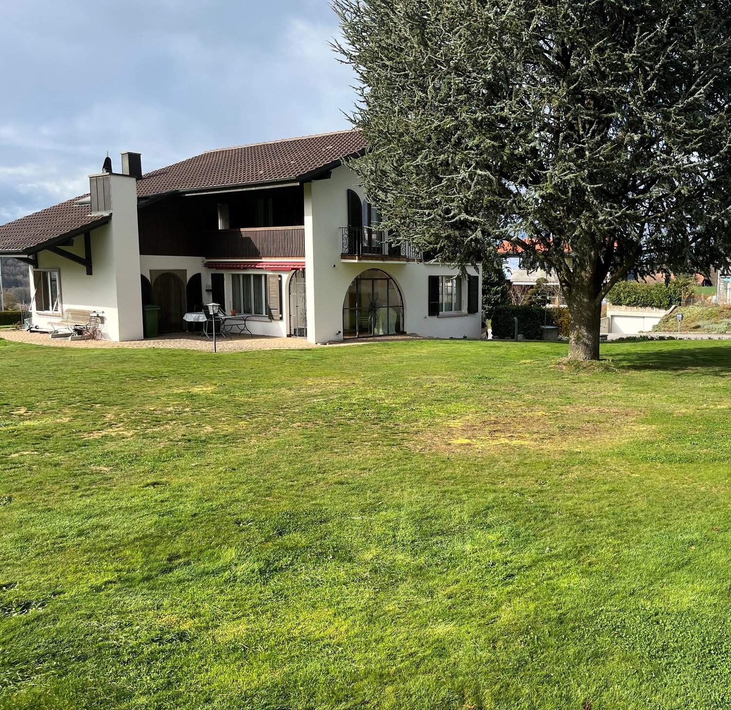 2 story house, brown roof, white walls, large windows, balcony, garden, tree