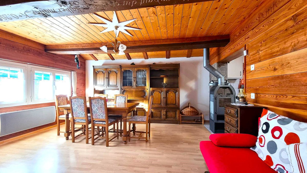 Rustic wooden interior with exposed beams, large wooden dining table and chairs, antique wooden cabinets, wood-burning stove, and decorative star-shaped light fixture