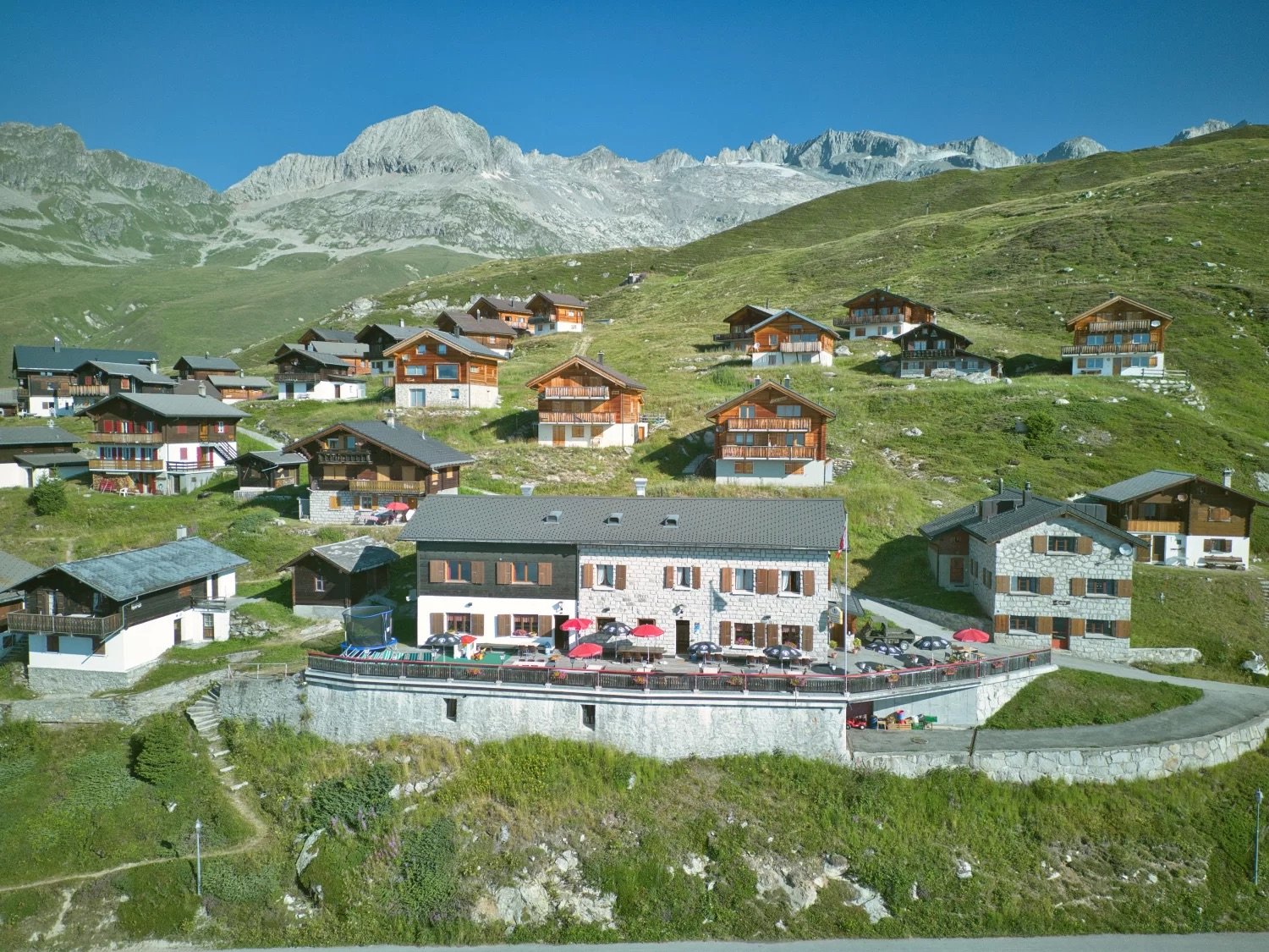 Collection of vacation houses, located on a hillside, surrounded by mountains, with an outdoor dining area.