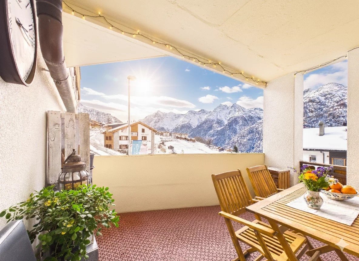 Balcony with wooden chairs, table, flowers, mountains in the background, sunny day