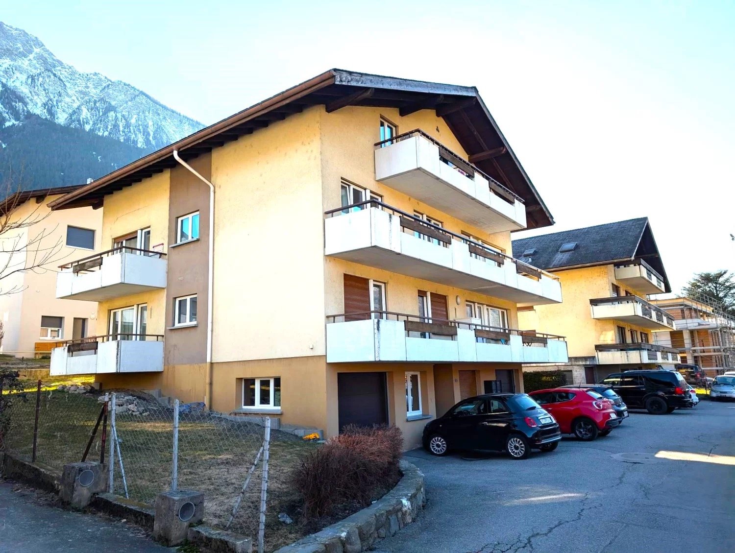 3 story building, yellow exterior, multiple balconies, garage, cars parked in front
