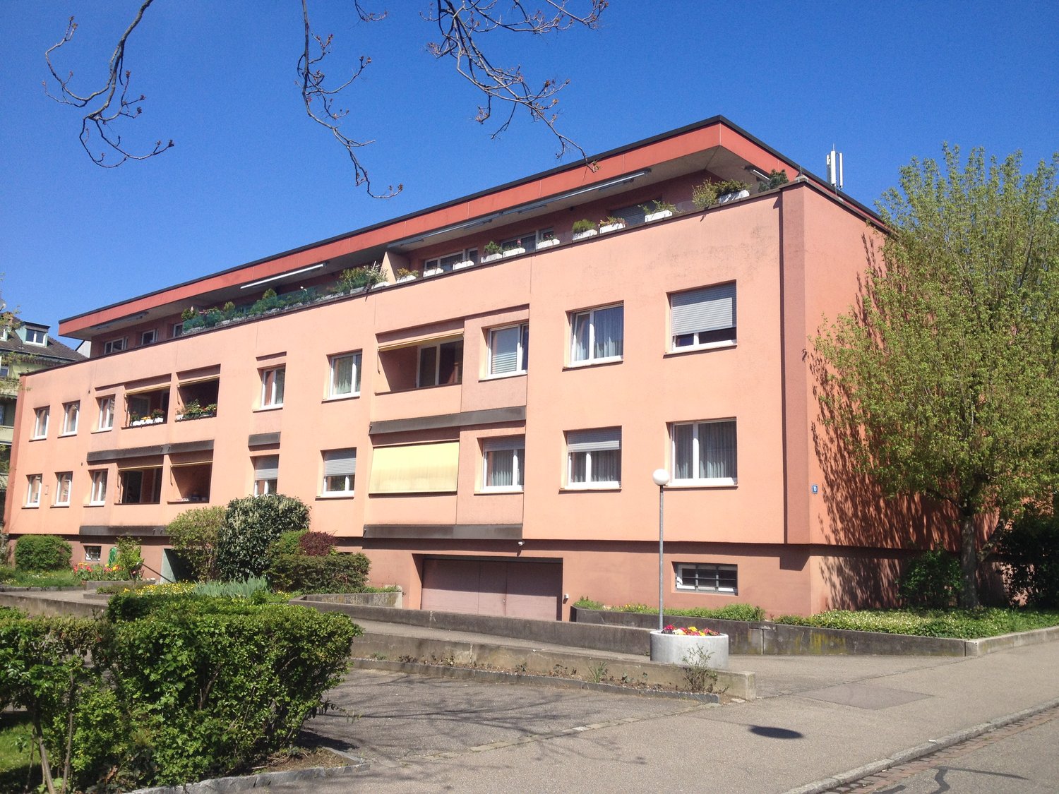 4 story building, pink exterior, multiple windows, garage, plants on the terrace