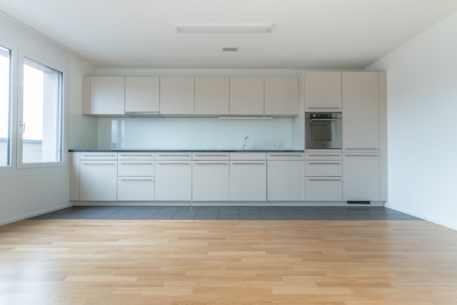 modern kitchen with white cabinets, wooden floor, large window, stainless steel oven, sink with faucet