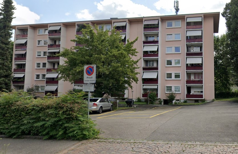 5 story apartment building, pink exterior, multiple balconies, parking lot, car parked