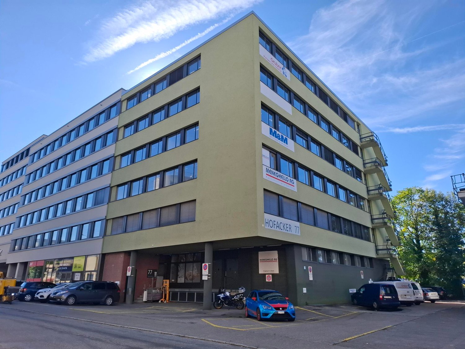 Multi-story office building, green exterior, several windows, parking area in front, staircases on side
