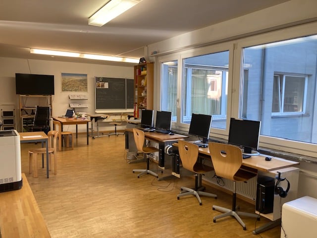 room with several wooden desks, chairs, monitors, shelves, and blackboard