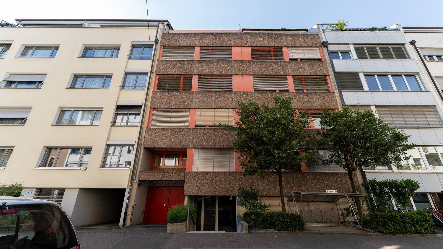 4 story building, red doors, multiple windows, beige and brown exterior, tree in front