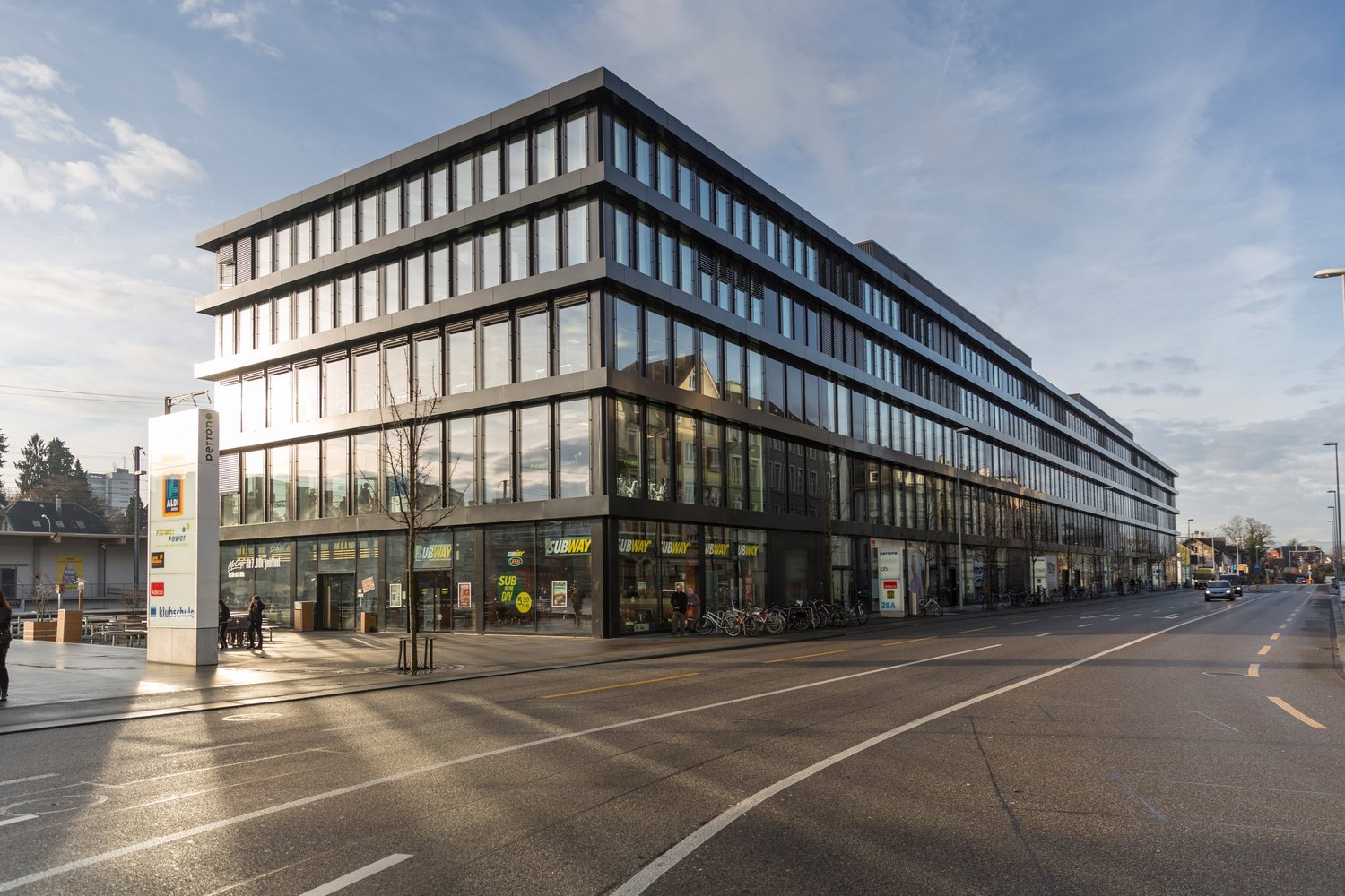 a four story office building, large windows, front sidewalk, multiple stores, bicycles parked