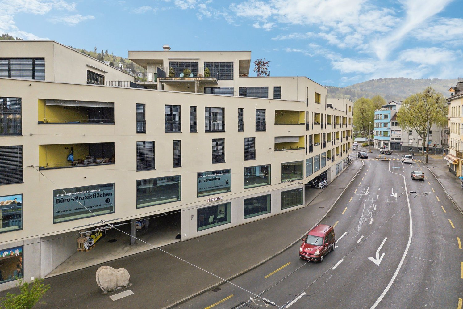 Modern multistory building, white walls, multiple garages, windows, balconies, visible mountain range