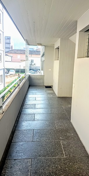 Hallway with tile flooring, white walls, and a balcony or terrace visible through the windows.