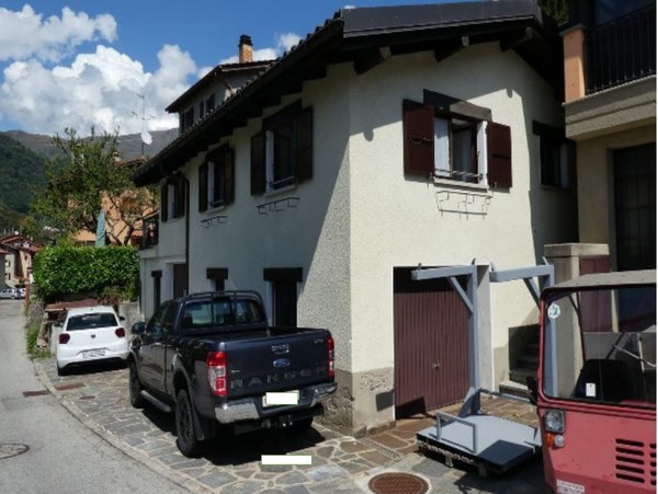 2-story house with white exterior walls, red shutters, and a garage with a parked vehicle in front of the house.