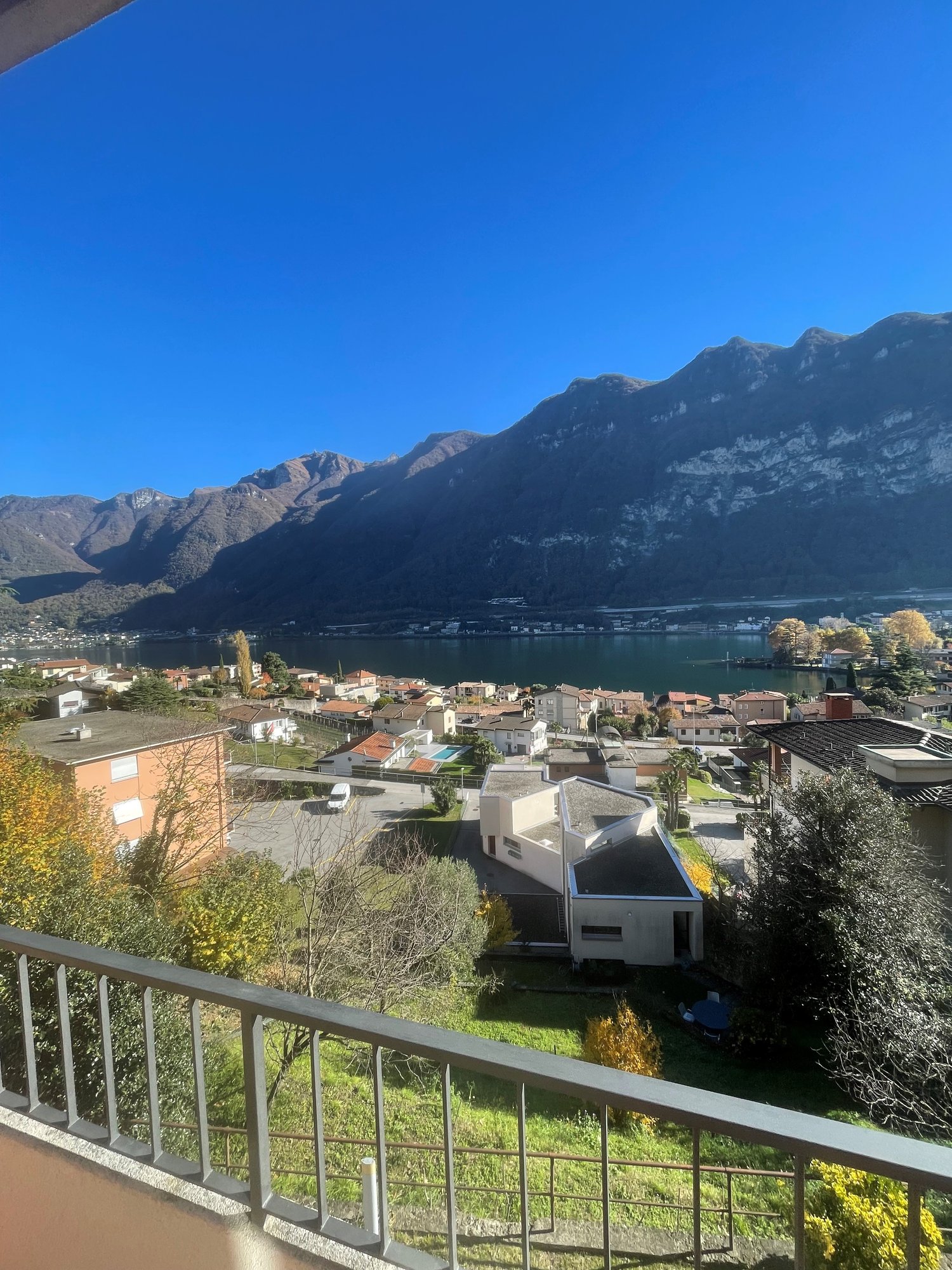View from a balcony overlooking a village with mountain range, lake, and sky.