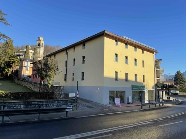 Yellow apartment building on a hill, many windows, stores at the bottom, street sign, sidewalk