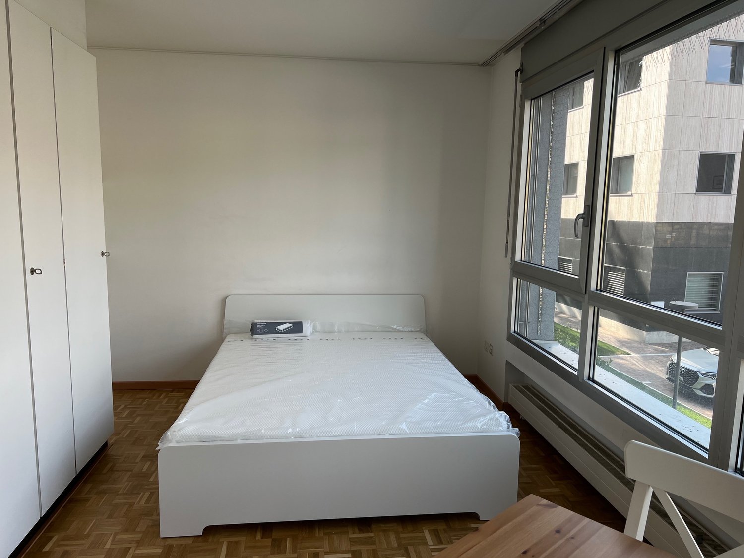 empty bedroom with white bed, white wardrobe, parquet floor, large windows