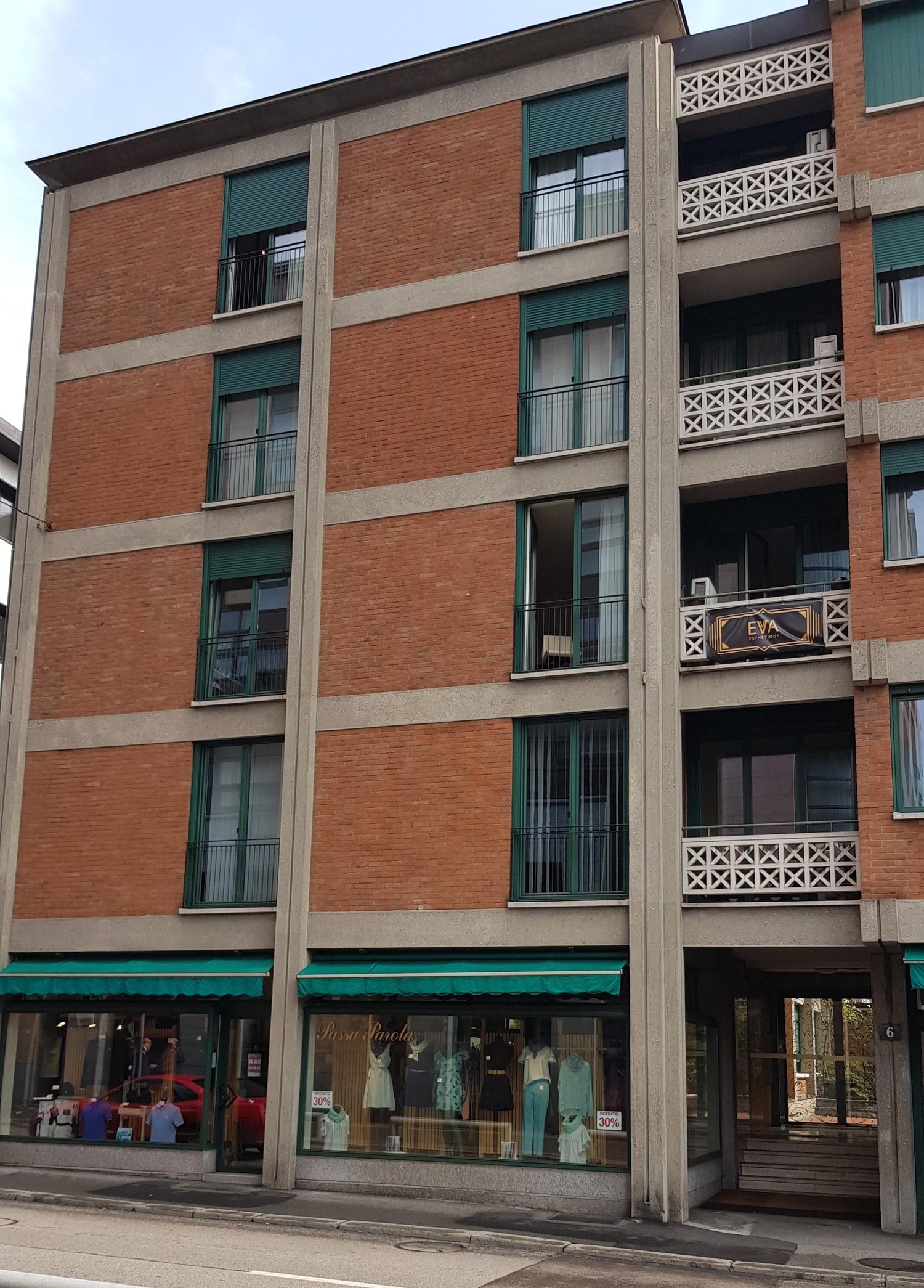 Red brick residential building, 4 stories, green windows, balconies, air conditioning units, ground floor stores