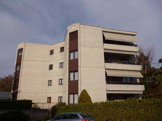 4-story apartment building with beige exterior, balconies, and a car parked in front