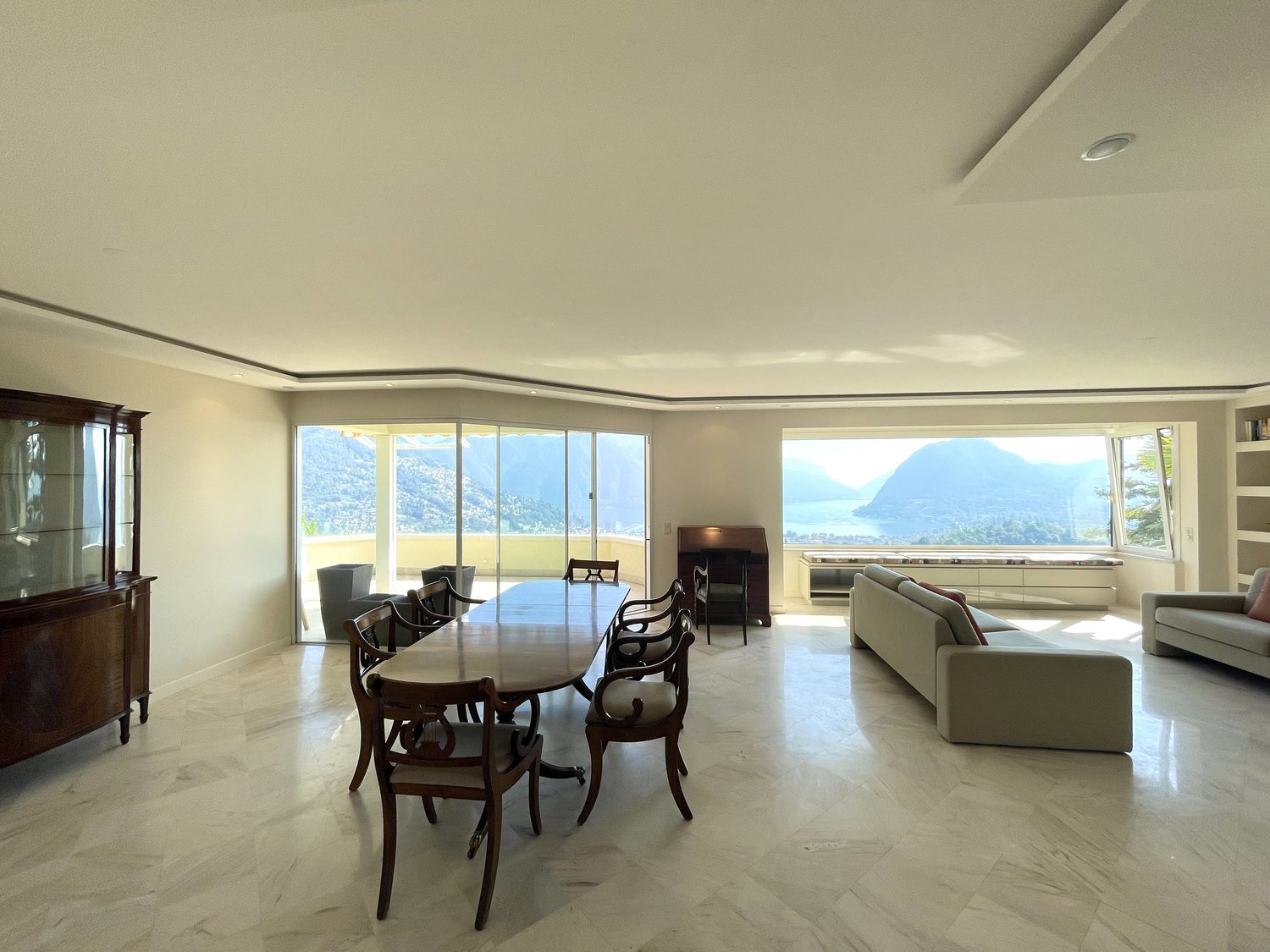 Spacious room with a dining table, chairs, a cabinet, a couch, an ottoman, a fireplace, and bookshelves. Large windows offer a scenic view.