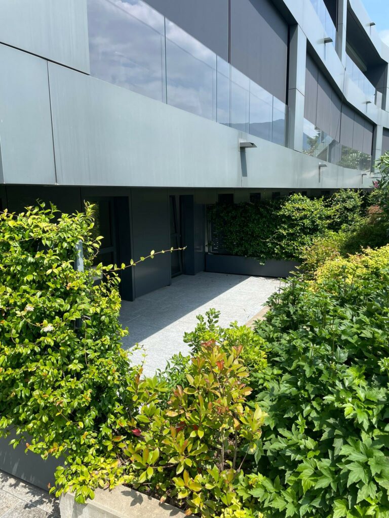 Modern apartment building, metallic facade, glass windows, greenery in the front