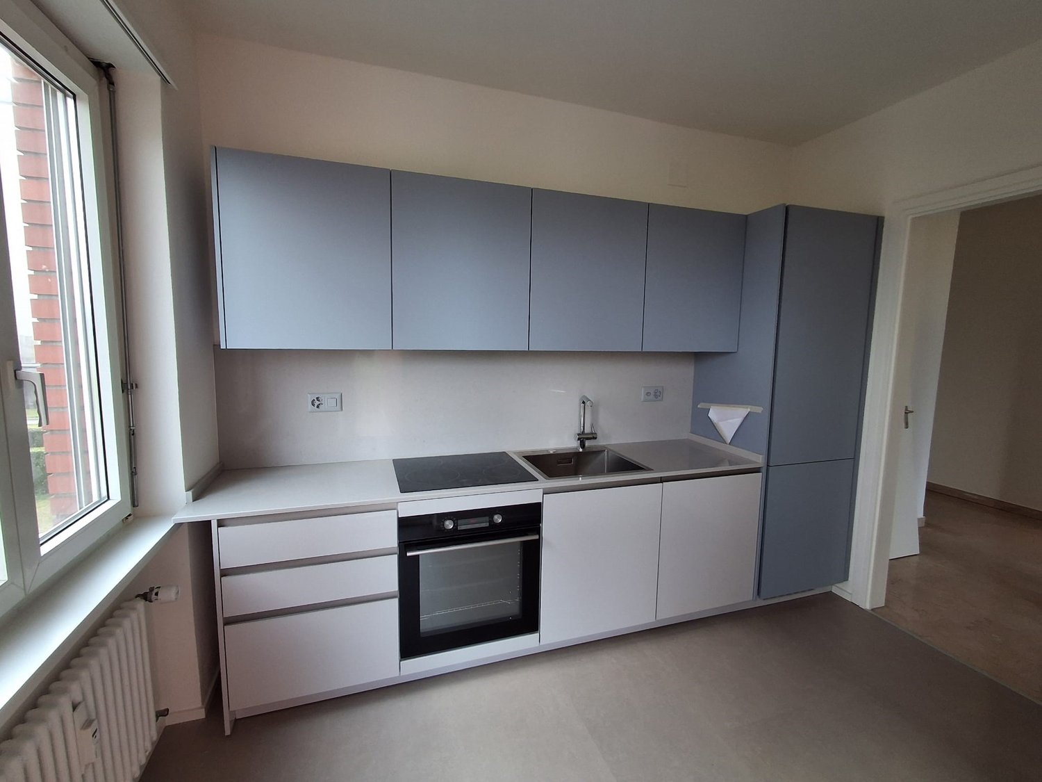 Modern kitchen with white cabinets, gray countertops, a sink, and a gas stove. The kitchen is equipped with a built-in oven and a towel hanging on the wall.