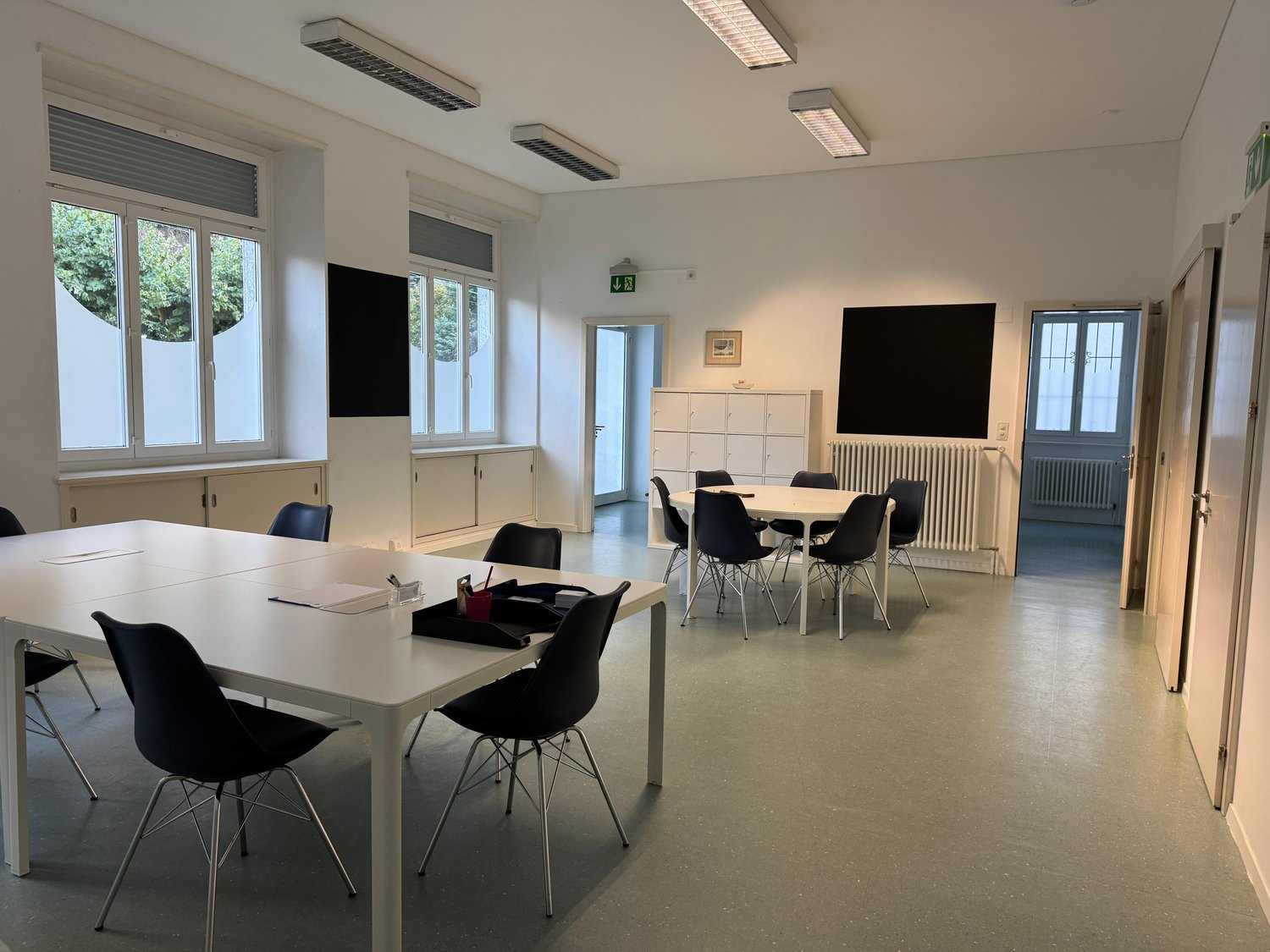 empty room, white walls, white tables, black chairs, windows, radiators, cabinets, blackboards