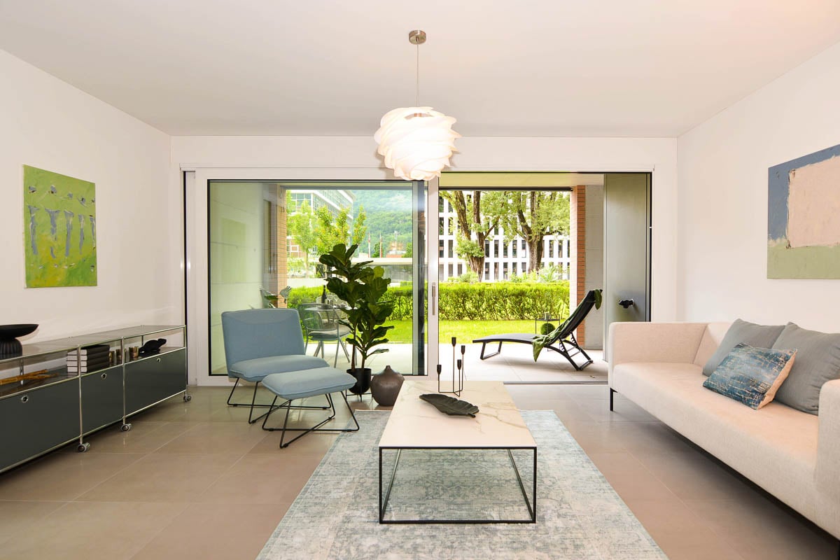 Living room, with sofa, center table, modern blue chairs, large glass doors leading to balcony, large paintings on the wall