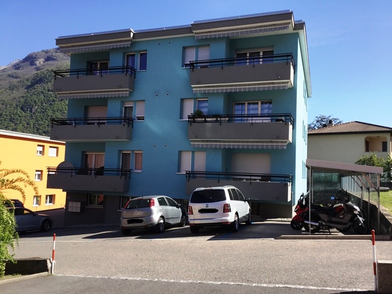 3-story apartment building with balconies, painted in a teal color, with cars parked in the front