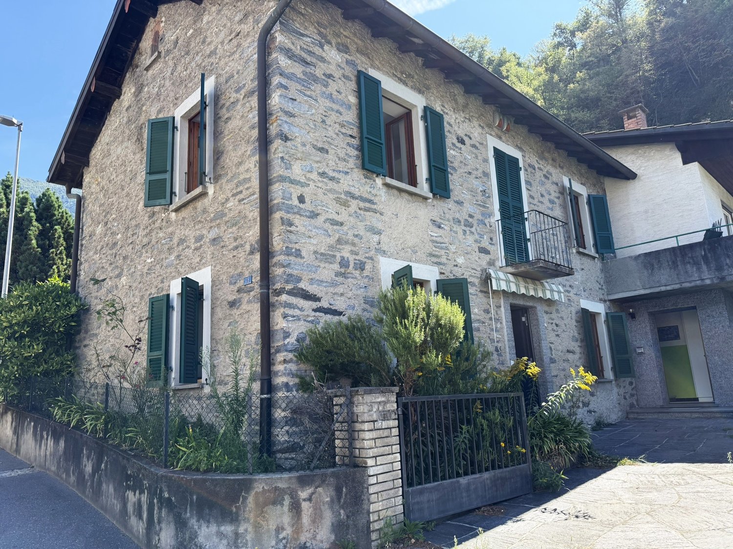 2-story stone house with green shutters, balcony, and landscaped garden in front