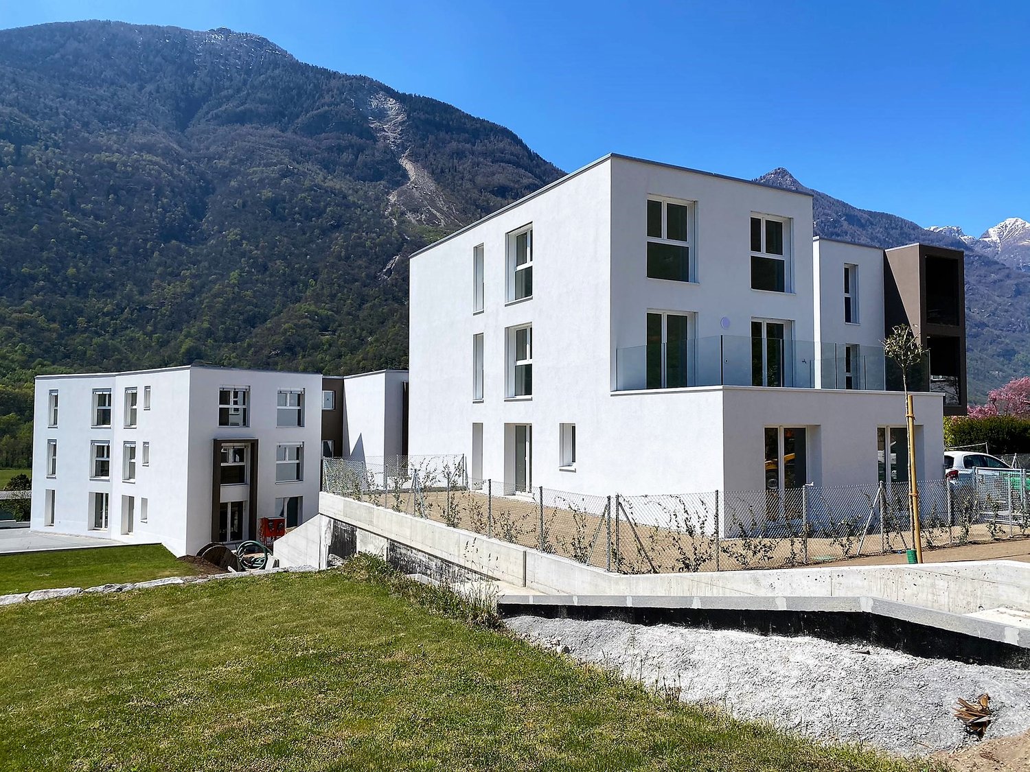 Modern white building, 4 stories, glass windows, metal railings, surrounded by mountains and greenery