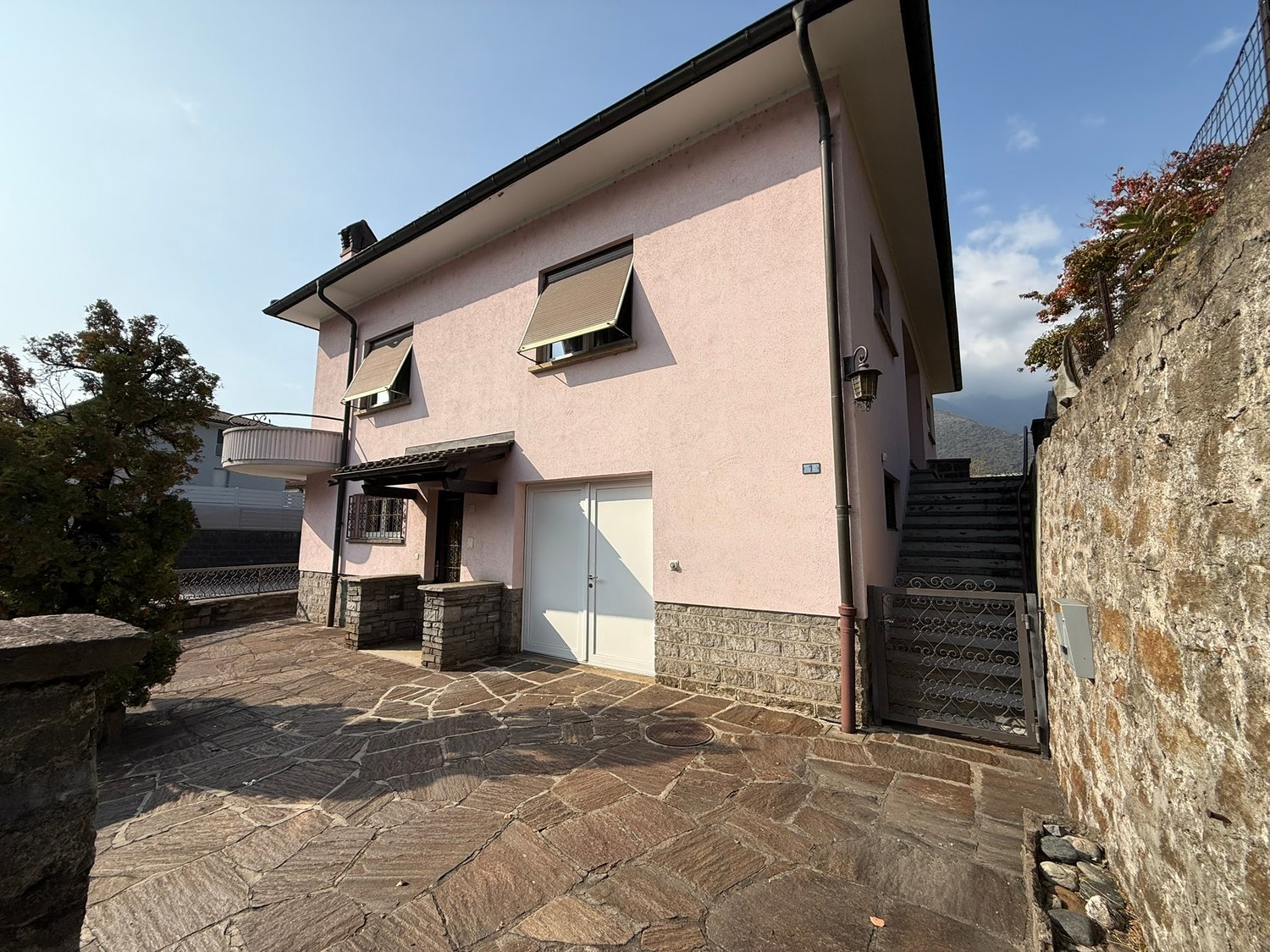 Two story house, pink exterior, white door, garage, stone walls, stairs, windows with awnings, outdoor patio