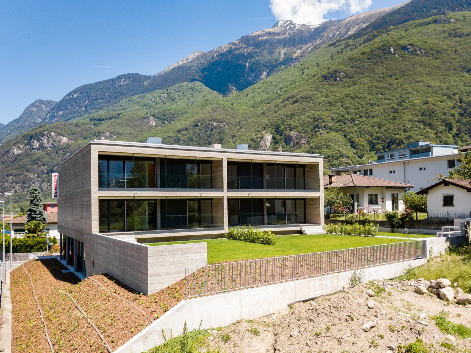 Modern architectural design, concrete and glass facade, large windows, surrounded by greenery, mountainous backdrop