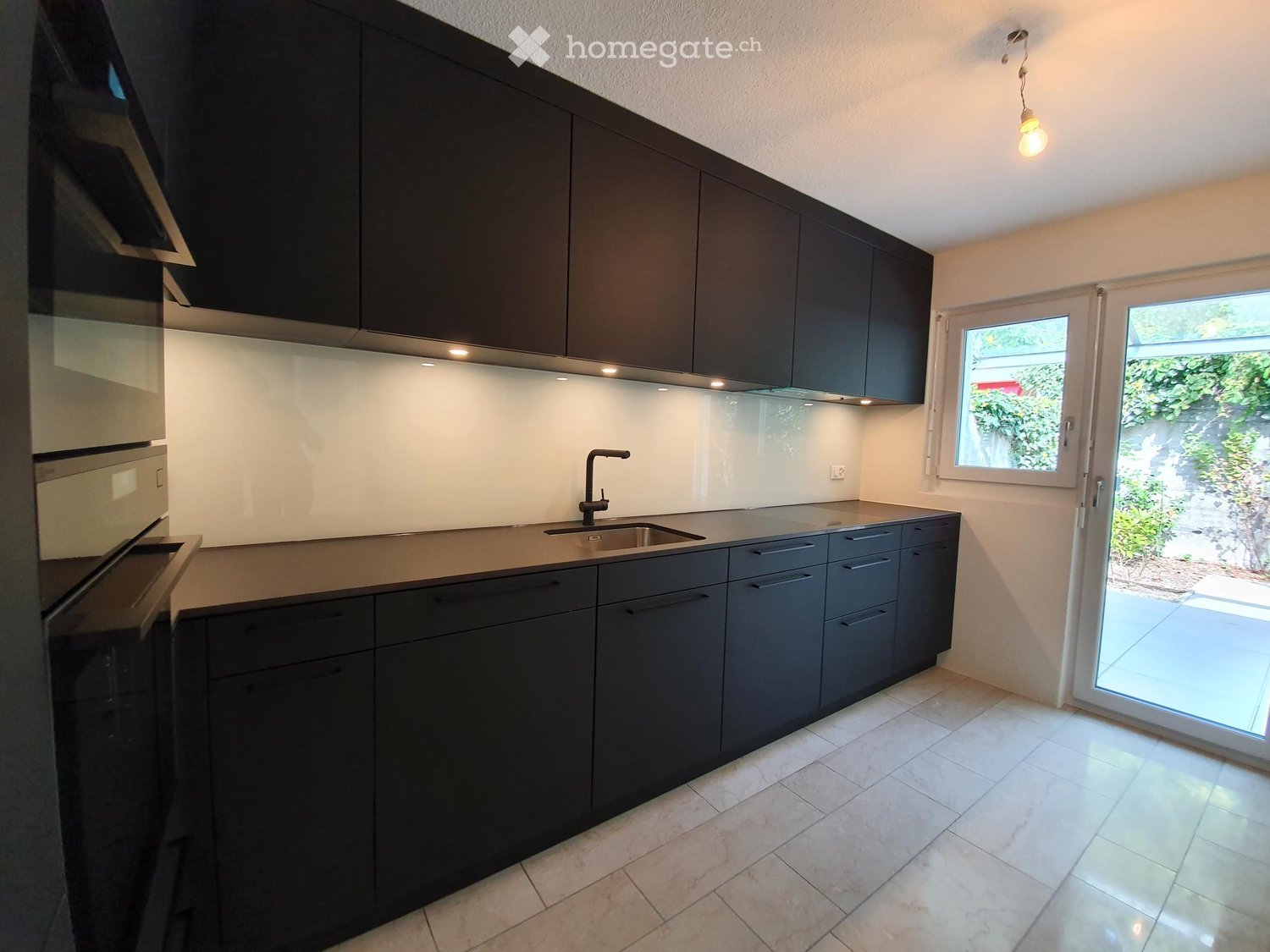 Modern kitchen with dark cabinets, white countertops, tile flooring, and a window overlooking the outdoor area. The kitchen is equipped with a sink and a dishwasher.