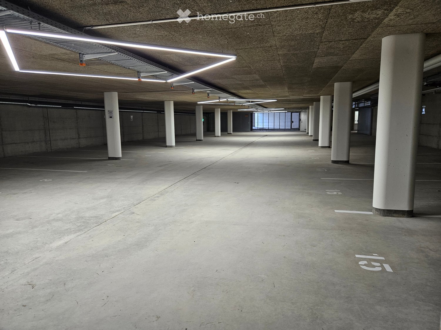 Underground parking space, square layout, illuminated by white ceiling lights, concrete floor, rows of vertical white pillars