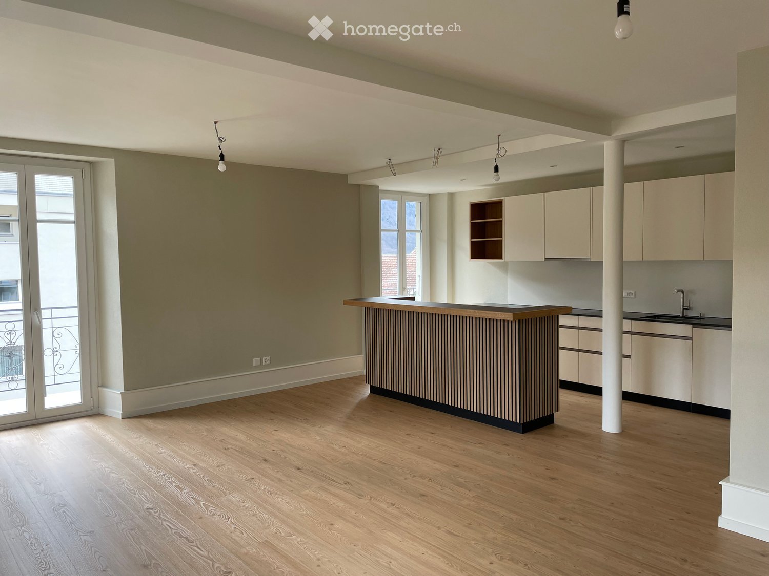Kitchen room with island counter, wooden floors, and sliding glass doors leading to a balcony with iron railing.