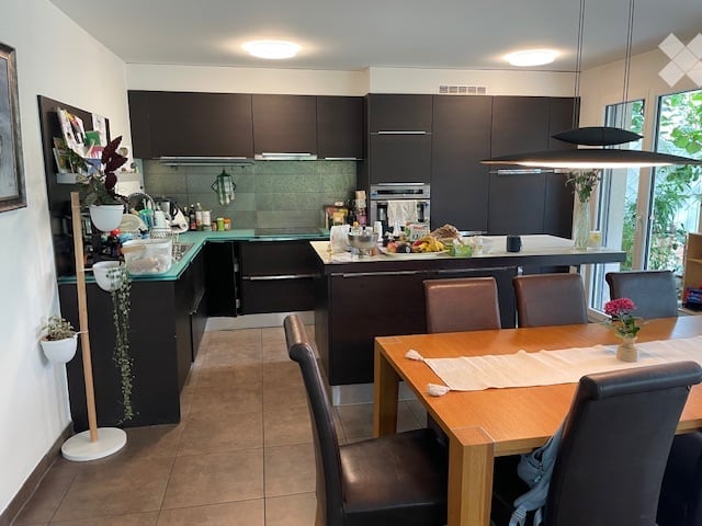 kitchen with dining area, wooden table, brown chairs, black cabinets, counter, white walls, green counter, potted plants, kitchen equipment
