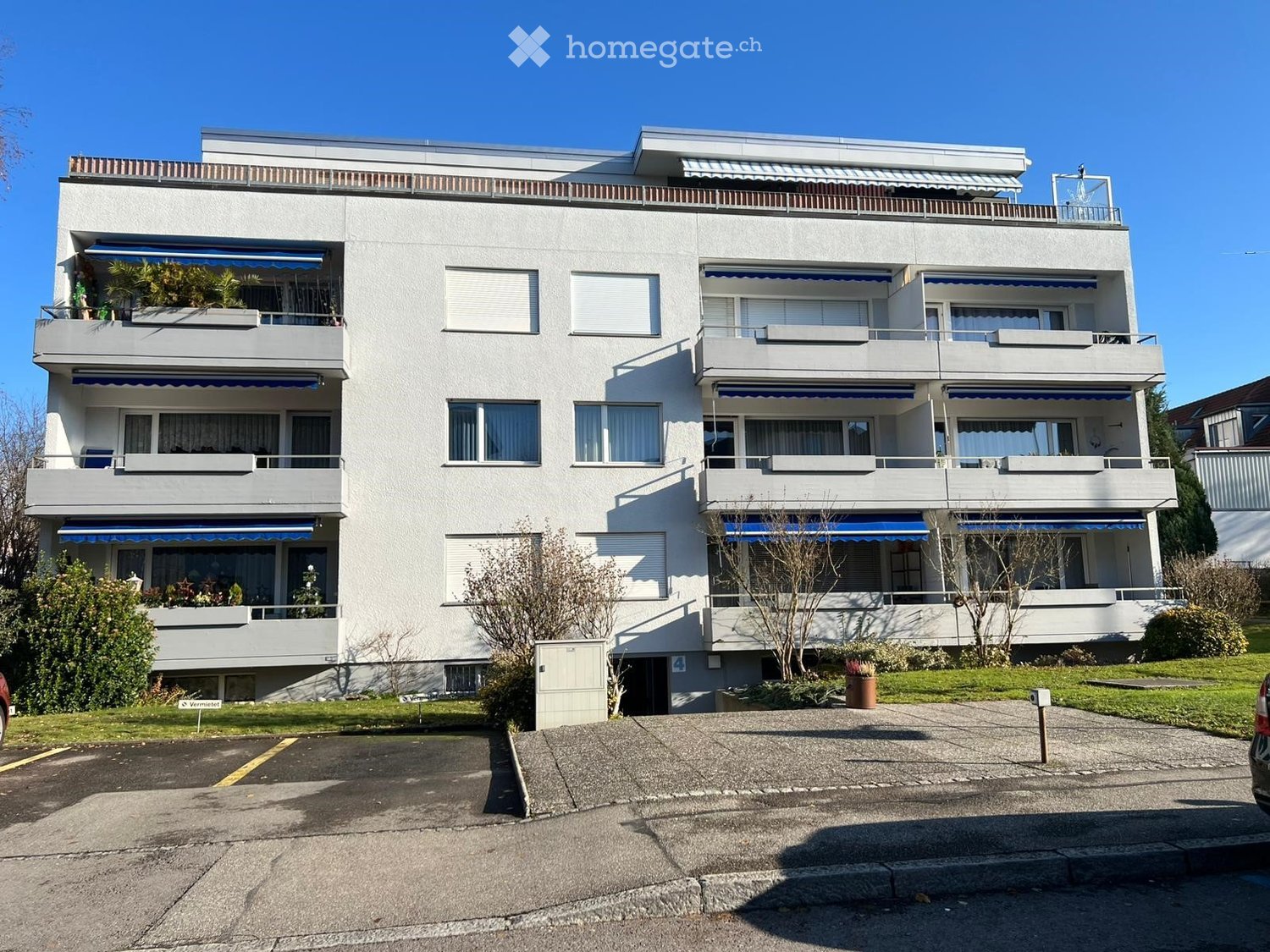 3 story apartment building, balconies, parking area, trees, shrubs