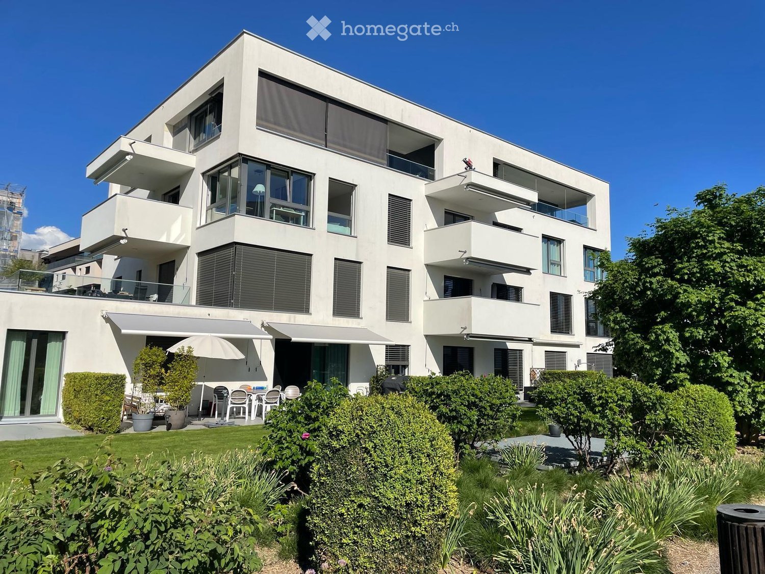 modern white apartment building with balconies, large windows, garden, green shrubs